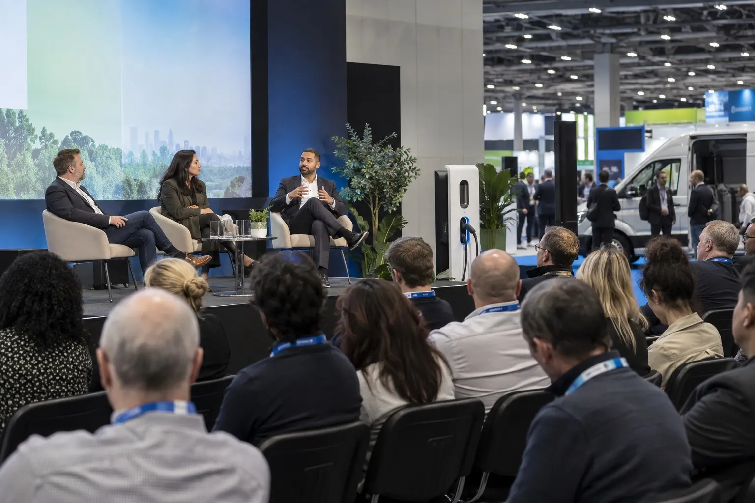 Illustrative electric-mobility conference discussion with delegates and an electric van