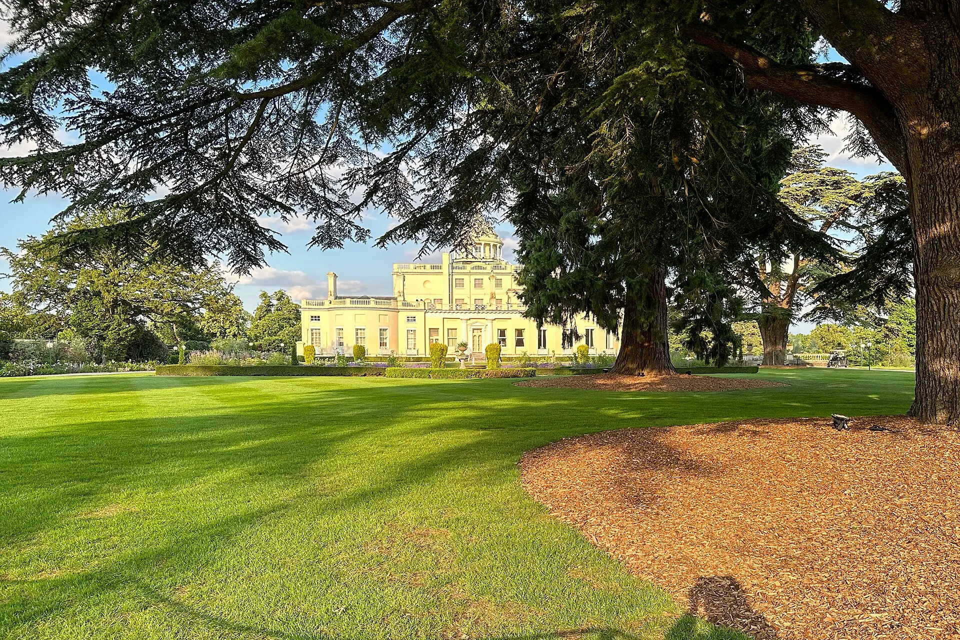 Stoke Park mansion seen across the lawn through mature trees in 2023